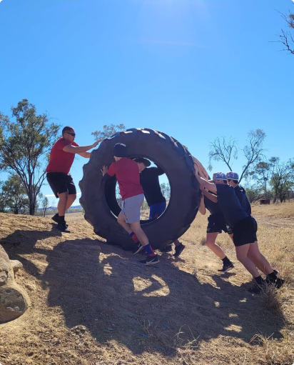 A team of people working together pushing a huge tyre up a dirt hill