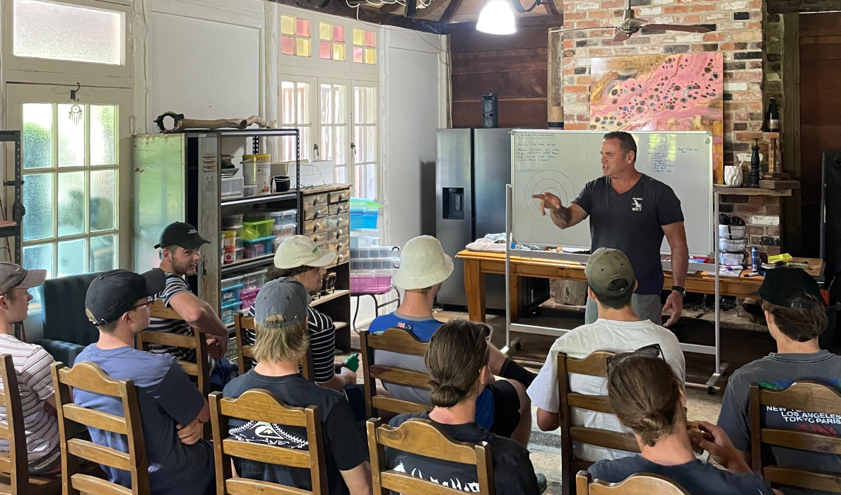 A group of people sitting, listening to a trainer in an indoor training room with a white board in the background