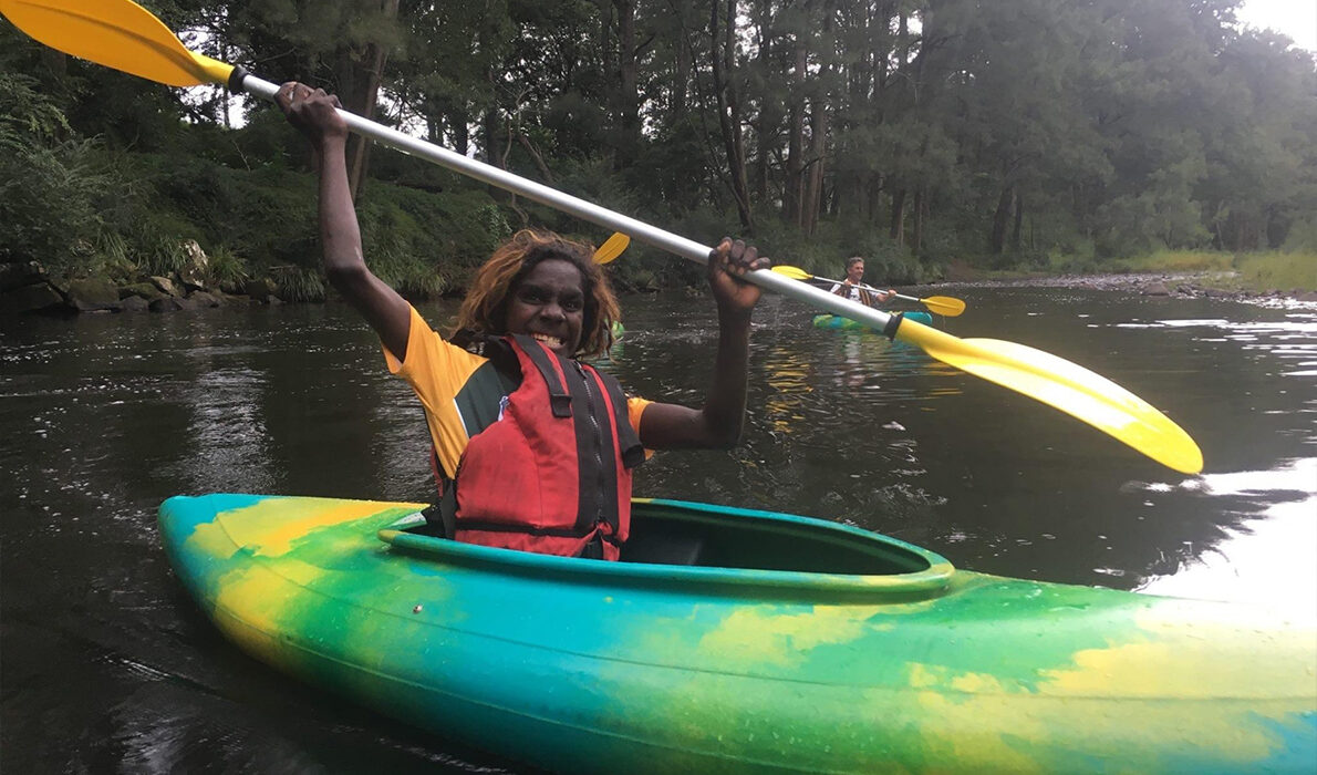 A happy child in a kayak on the water smiling and holding up their oar