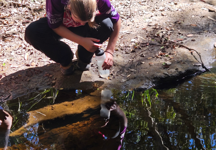 A person looking at the waters edge, kneeling observing nature